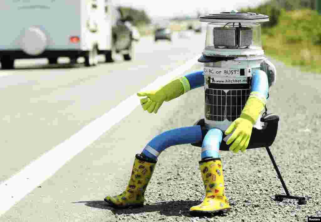 The anthropomorphic robot named hitchBOT sits on the shoulder of Highway 102 to begin its 6,000 kilometer cross country journey outside of Halifax, Nova Scotia, July 27, 2014. The hitch- hiking robot is part of a social experiment to see if drivers will pick up and drop off the robot in one piece to an art gallery in Victoria, British Columbia.