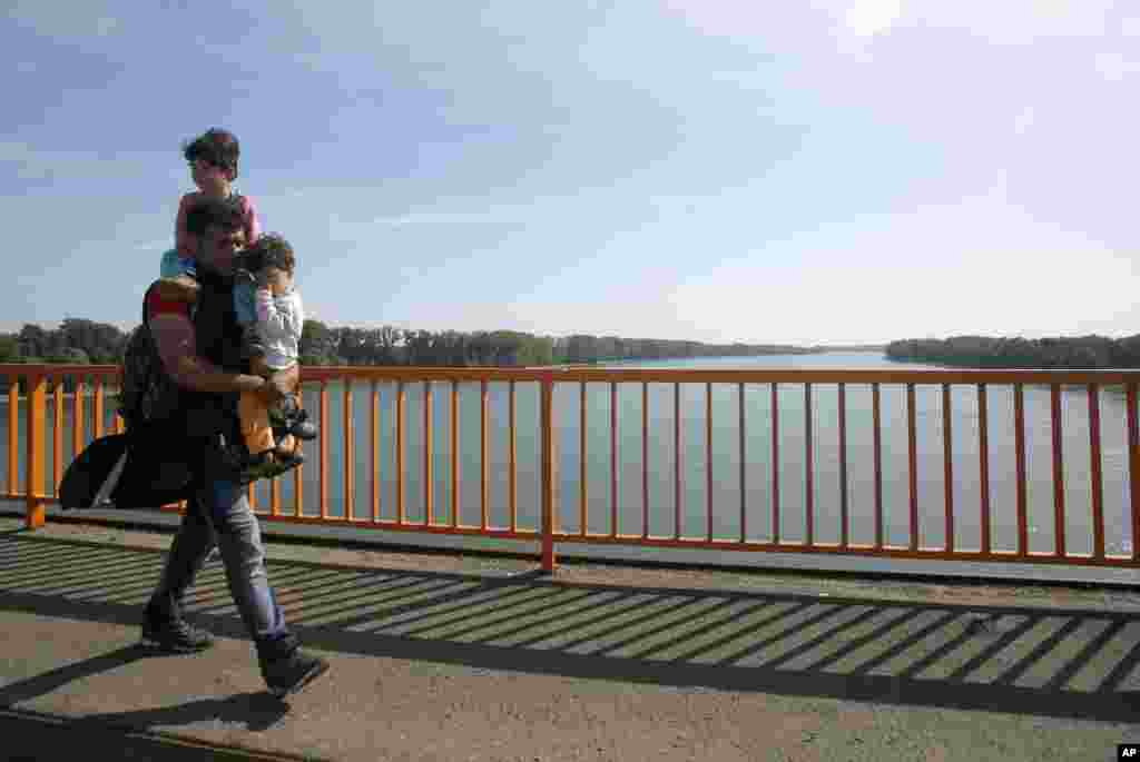 A man carrying two children walks along a bridge over the Danube river between Serbia and Croatia, near Batina.
