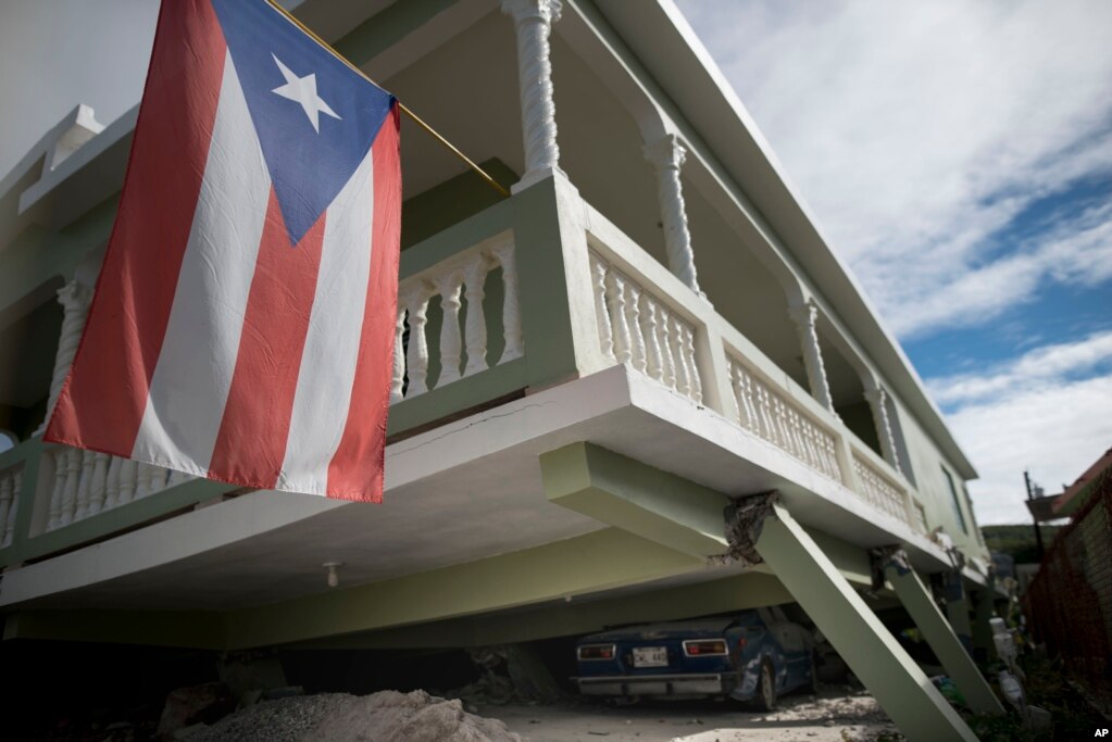 Una bandera puertorriqueña cuelga del porche de una casa que se derrumbó encima de automóviles estacionados después de un terremoto en Guánica, Puerto Rico, el lunes 6 de enero de 2020.