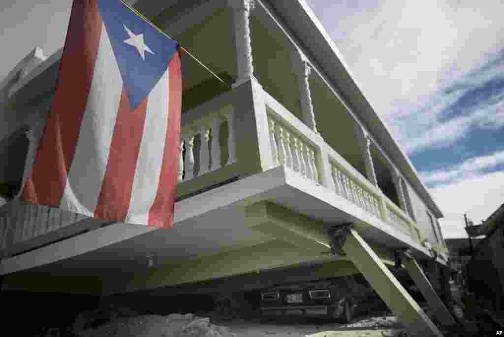 Una bandera puertorriqueña cuelga del porche de una casa que se derrumbó encima de automóviles estacionados después de un terremoto en Guánica, Puerto Rico, el lunes 6 de enero de 2020.
