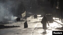 A woman walks in the rain in front of a checkpoint in the rebel held area of Aleppo's Seif al-Dawla district, Syria, March 28, 2016. Both rebels and government forces have been accused of using chemical weapons.