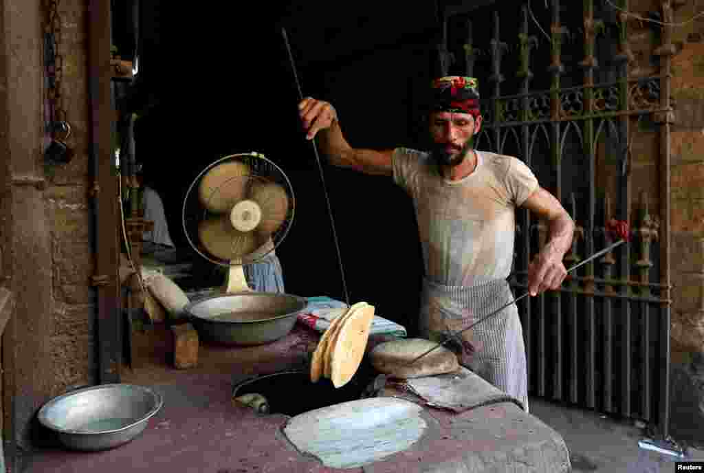 A worker collects bread from the oven while preparing and selling them at the entrance of a building in Karachi, Pakistan.