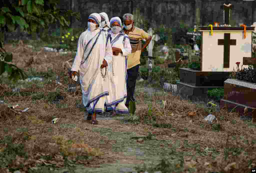 Nuns of the Missionaries of Charity, the order founded by Saint Teresa, wearing face masks as a precaution against the coronavirus walk along the graves of the deceased during All Souls Day in Kolkata, India, Monday, Nov. 2, 2020. (AP Photo/Bikas Das)