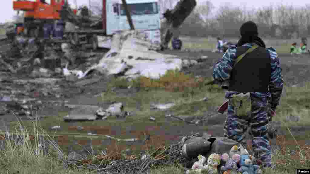Pria bersenjata pro-Rusia, dengan tumpukan boneka binatang di kakinya, mengumpulkan puing-puing pesawat Malaysia Airlines MH17 dekat daerah permukiman Grabovo, Donetsk, Ukraina timur (16/11).&nbsp;(Reuters/Antonio Bronic)