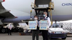 In this photo released by the Taiwan Centers for Disease Control, Taiwan's Health Minister Chen Shih-chung, left, and Brent Christensen, the top U.S. official in Taiwan, hold up thank you cards as they welcome a China Airlines cargo plane carrying COVID-1