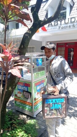 Seorang tukang perbaikan jam keliling sedang mengambil sebungkus nasi gratis. (Foto: Courtesy)