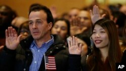 Weizhen Cai from China, right, and Ahmed Haloui from Morocco recite the oath of citizenship during a celebration of the naturalization off approximately 200 new citizens of the United States, Nov. 30, 2017 at the John F. Kennedy Library in Boston.