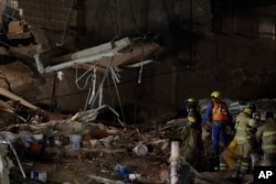 Rescue workers use a crane to lift a section of concrete floor as they remove rubble in hopes of reaching dozens of people believed to be trapped inside a collapsed office building since a 7.1 magnitude earthquake, in the Roma Norte neighborhood of Mexico City, just after midnight Sept. 25, 2017.