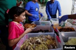 Seorang anak perempuan menerima makanan dari “Dapur Keluarga” yang mengemas makanan berlebih dari hotel bintang lima dan membagikan kepada masyarakat miskin selama Ramadan, di kamp Palestina Al-Baqaa, dekat Amman, Yordania, 11 Juni 2018.