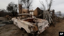 A truck is burnt out and a house destroyed at Conjola Park, Australia, Sunday, Jan. 5, 2020, after recent wildfires ripped through the community. (AP Photo/Rick Rycroft)