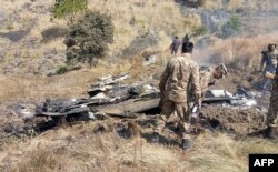FILE - Pakistani soldiers stand next to what Pakistan says is the wreckage of an Indian fighter jet shot down in Pakistan-controlled Kashmir at Somani area in Bhimbar district near the Line of Control, Feb. 27, 2019.