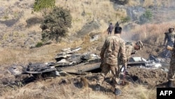 Serdadu-serdadu Pakistan berdiri dekat apa yang diklaim oleh Pakistan sebagai reruntuhan pesawat tempur India yang ditembak jatuh di Kashmir di kawasan Somani di distrik Bhimbar yang berada di bawah kendali Pakistan, 27 Februari 2019 (foto: STR/AFP)