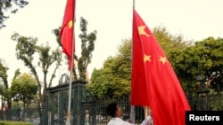 资料照：中越外长在河内举行会谈前，一名男子在越南政府办公机构前竖起的越南国旗旁升起中国国旗。（2017年11月2日）