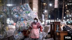 Una mujer, usando mascarilla y una bolsa plástica como protección, traslada bolsas con desechos reciclables en Manhattan, Nueva York, en plena pandemia.