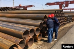 FILE - Workers inspect steel pipes at a steel mill of Hebei Huayang Steel Pipe Co Ltd in Cangzhou, Hebei province, China, March 19, 2018.