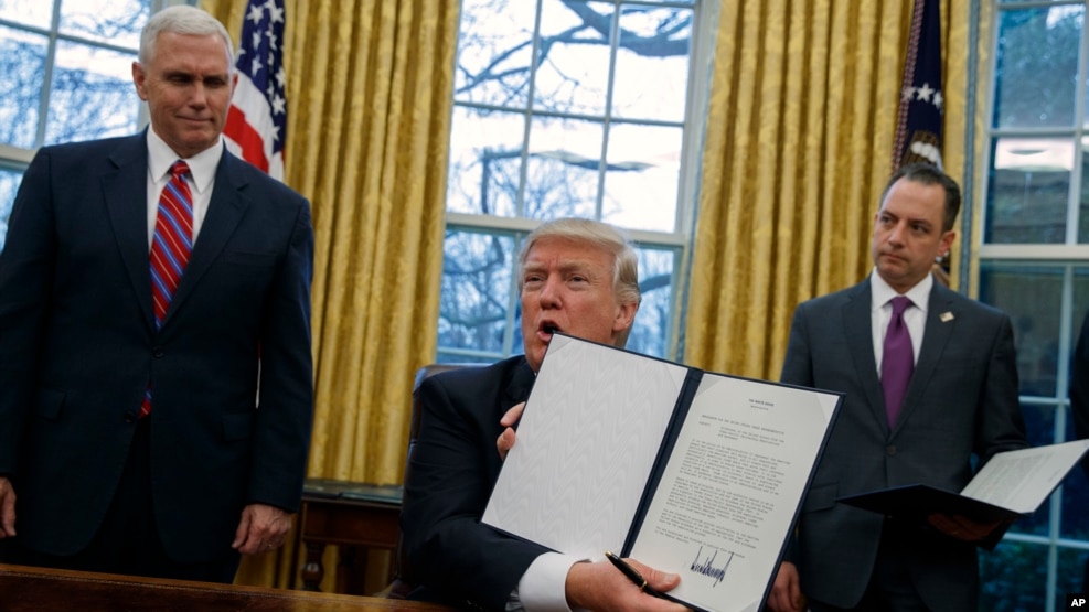 美国副总统彭斯（左）和白宫办公厅主任普里巴斯（右）目视总统川普展示宣布美国退出TPP的行政令。（2017年1月23日）
