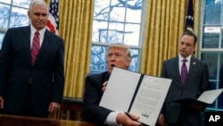 FILE - Vice President Mike Pence, left, and White House Chief of Staff Reince Priebus watch in the Oval Office as President Donald Trump shows off an executive order to withdraw the U.S. from the Trans-Pacific Partnership trade pact, Jan. 23, 2017.