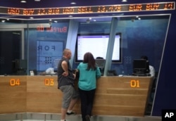 FILE - A man and woman stand below a ticker at the counter of a foreign currency exchange bureau at Johannesburg's OR Tambo International Airport, Aug. 24, 2015.