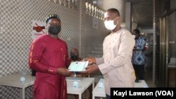 Le SG du SYNJIT, Isidore Kouwonou, remettant la carte d’assuré au journaliste Kossi Balao, à Lomé, 14 avril 2021. (VOA/Kayi Lawson)