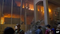 In this photo taken on a government organized tour, soldiers and civilians gather in front of a burning official building following an airstrike in Tripoli, Libya, May 17, 2011