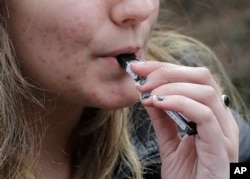 FILE - A high school student uses a vaping device near a school campus in Cambridge, Massachusetts.