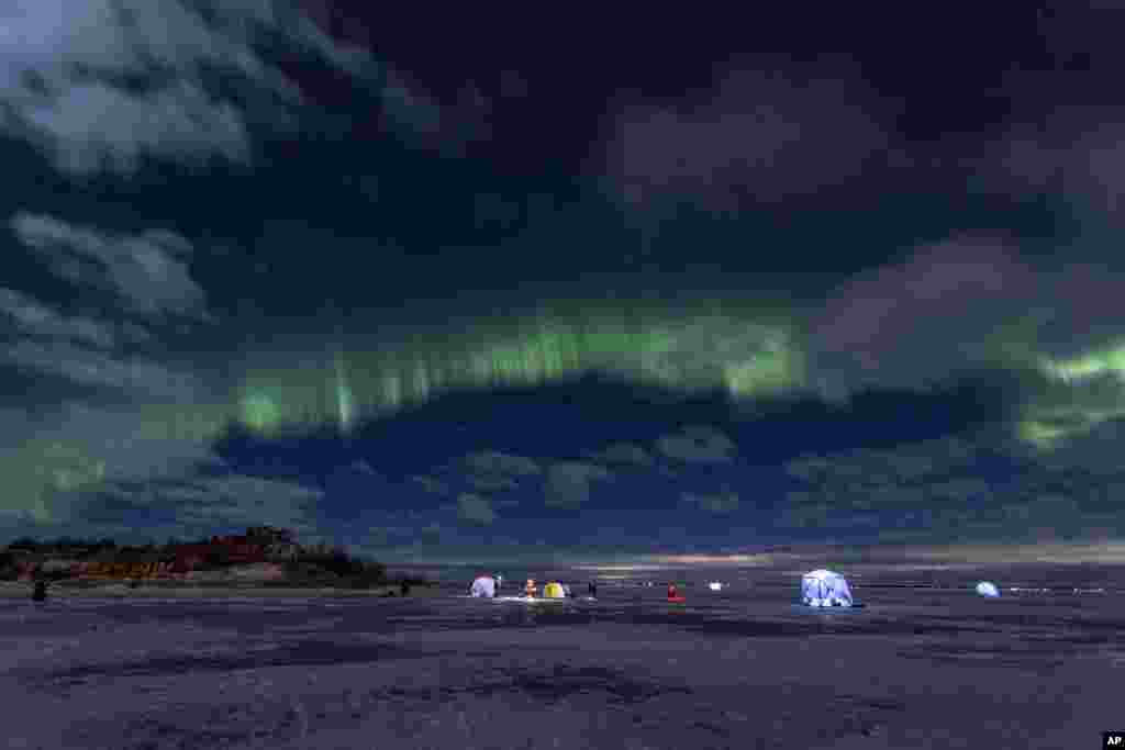 The northern lights, or aurora borealis, illuminate the night sky above fishermen on the ice of Finnish Gulf outside St. Petersburg, Russia, Jan. 15, 2022.