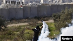 A Palestinian stone-throwing protester uses a sling to throw back a tear gas canister fired by Israeli security officers (rear) during clashes in the West Bank village of Bilin near Ramallah, January 4, 2013. 