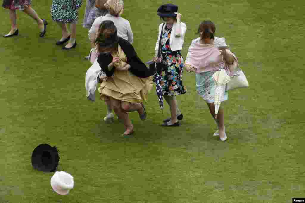 Para perempuan mengejar topi mereka yang ditiup angin kencang di pesta kebun di Istana Buckingham di tengah kota London, Inggris.