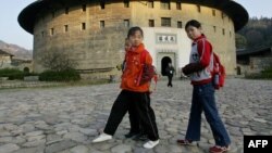 FILE - Schoolchildren pass by an old circular Tulou earth house, which are the traditional homes of China's minority Hakka people, in Yongding village, Fujian Province, December 15, 2005.