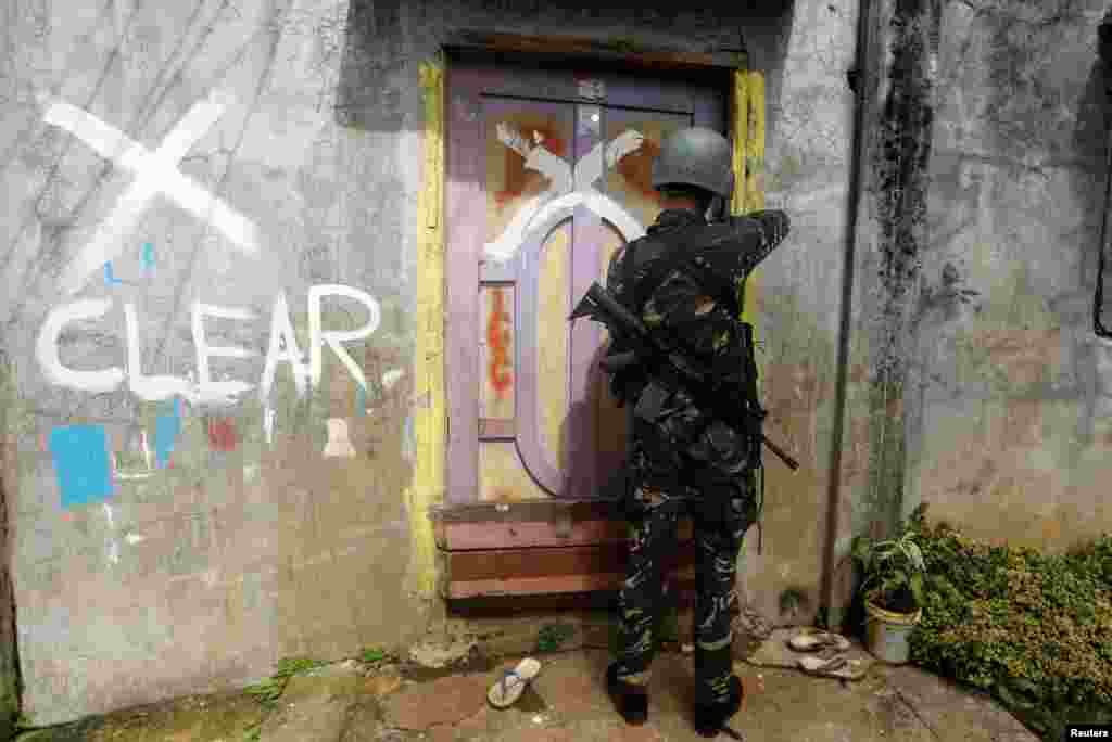 A member of the Philippine National Police (PNP) closes a door after marking a house as clear while government troops continue their assault against insurgents from the Maute group in Marawi city.