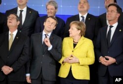 French President Emmanuel Macron, front second left, and German Chancellor Angela Merkel, front second right, look up at a drone flying over their heads during a group photo at an EU summit at the Europa building in Brussels, Dec. 14, 2017.