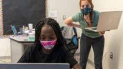 In this Tuesday, Sept. 29, 2020, photo English Language Arts teacher Rebecca Ain, right, helps a student in her class at The Social Justice Public Charter School, in Washington. (AP Photo/Jacquelyn Martin)