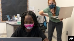 In this Tuesday, Sept. 29, 2020, photo English Language Arts teacher Rebecca Ain, right, helps a student in her class at The Social Justice Public Charter School, in Washington. (AP Photo/Jacquelyn Martin)