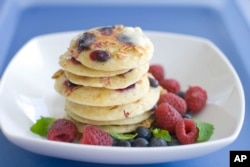 A plate of pancakes made with blueberries and granola with raspberries on the sides. (File Photo)