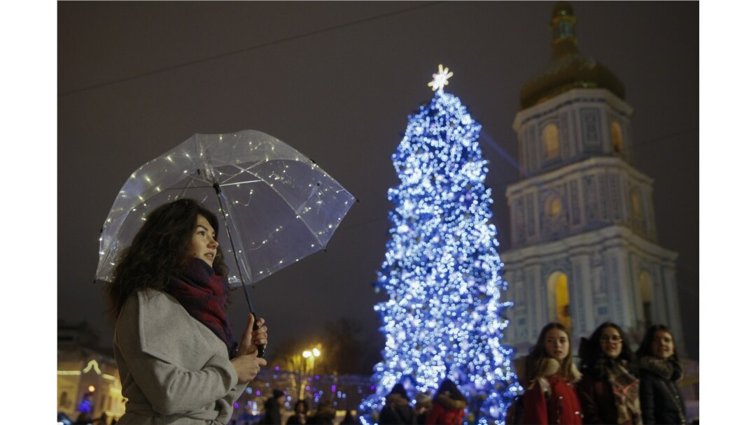 Seorang wanita berdiri di bawah payung yang dihiasi dengan lampu di dekat pohon Natal di pusat Kiev, Ukraina. (Foto: REUTERS/Valentyn Ogirenko)