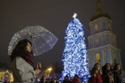 Seorang wanita berdiri di bawah payung yang dihiasi dengan lampu di dekat pohon Natal di pusat Kiev, Ukraina. (Foto: REUTERS/Valentyn Ogirenko)