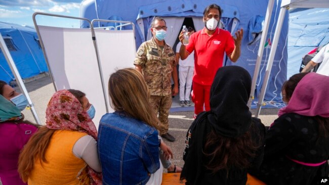 FILE - Afghan refugees listen to instructions before getting COVID-19 vaccine shots in an Italian Red Cross refugee camp, in Avezzano, Italy, Aug. 31, 2021.