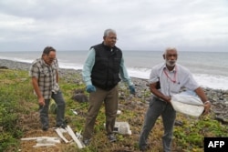 A Malaysian expert, center, looks for debris from the ill-fated Malaysia Airlines flight MH370 on a beach in Saint-Andre de la Reunion, on Reunion Island, in the Indian Ocean, Aug. 4, 2015.