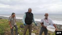 A Malaysian expert, center, looks for debris from the ill-fated Malaysia Airlines flight MH370 on a beach in Saint-Andre de la Reunion, on Reunion Island, in the Indian Ocean, Aug. 4, 2015. 