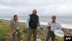 A Malaysian expert, center, looks for debris from the ill-fated Malaysia Airlines flight MH370 on a beach in Saint-Andre de la Reunion, on Reunion Island, in the Indian Ocean, Aug. 4, 2015.