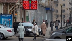 Warga berjalan di papan elektronik di Moskow yang menunjukkan nilai mata uang Rusia Rubel terus menurun ke rekor terendah (1/12).