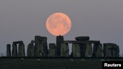 FILE - Sheep graze as the full moon, known as the "Super Pink Moon", sets behind Stonehenge stone circle near Amesbury, Britain, April 27, 2021.