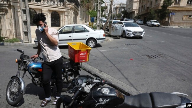 El repartidor de comestibles Saeed Vatanparast, con una máscara facial protectora para ayudar a prevenir la propagación del coronavirus, habla por su teléfono celular frente a una tienda en Teherán, Irán, el martes 21 de abril de 2020.