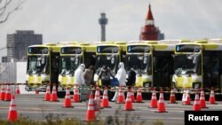 日本橫濱港裡身穿防護服的工作人員幫助鑽石公主號的乘客下船後搭乘大巴車離開。（2020年2月19日）