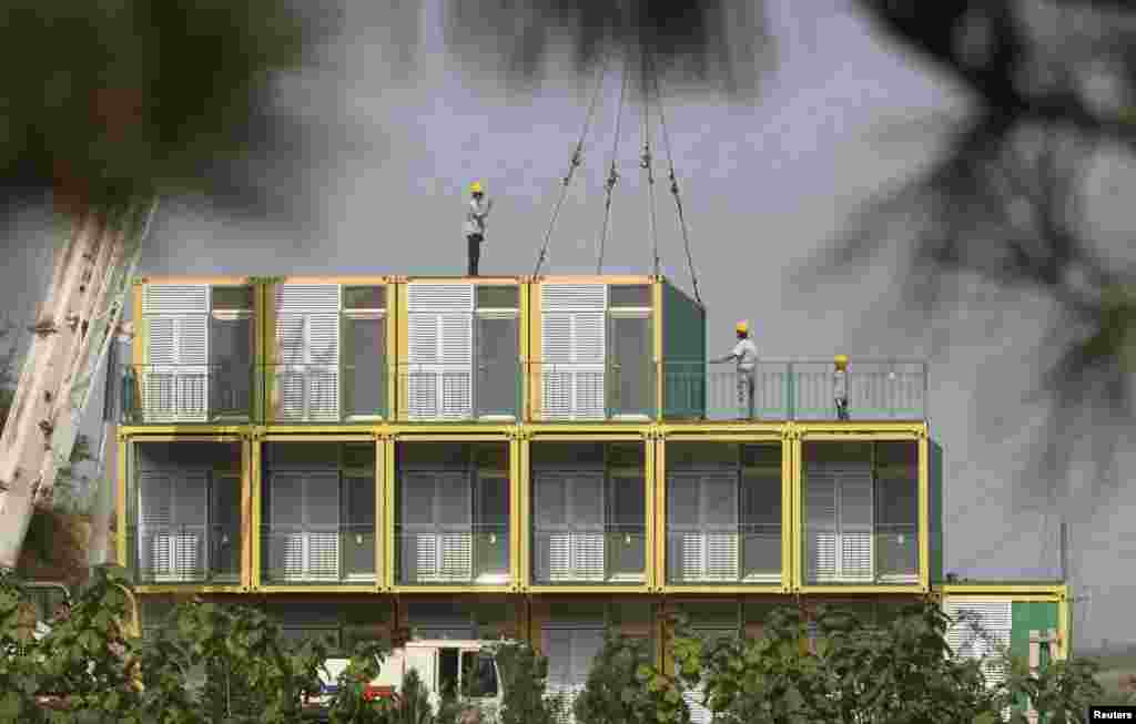 Workers guide a crane to position a shipping container as they build a hotel by piling up shipping containers at a tourism resort in Yantai, Shandong province, China.&nbsp;