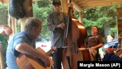 In this Oct. 12, 2017 photo, Mike Baughman, center, plays the bass with Sam Gibson, left, on guitar while Ryan Baughman, right, looks on at a cabin in Herald, W.Va. Mike Baughman is fighting a rare bile duct cancer he believes is a result of ingesting a parasite inside raw fish while serving in the Vietnam War. (AP Photo/Margie Mason)