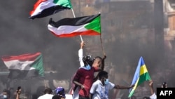 Sudanese demonstrators raise national flags as they take part in a protest in the city of Khartoum Bahri, the northern twin city of the capital, to demand the government's transition to civilian rule, Oct. 21, 2021.