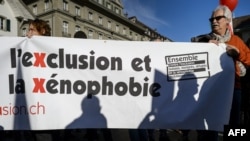 FILE - A man holds a banner reading in French "Together against exclusion and xenophobia, Swiss, immigrants, refugees let us unite!" during a demonstration in Bern against an initiative that wants to curb immigration and promote birth control in developing countries, Nov. 1, 2014. 