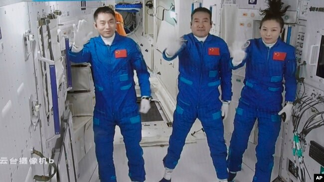 A screen grab taken at Beijing Aerospace Control Center in Beijing, China, Oct. 16, 2021, and released by Xinhua News Agency, shows three Chinese astronauts waving after they entered China's Tiangong space station core module Tianhe.