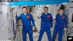 Potongan gambar yang diambil dari video di Pusat Kontrol Luar Angkasa Beijing, China, menunjukkan tiga astronaut asal China melambaikan tangannya saat mereka memasuki Stasiun Luar Angkasa Tiangong pada 16 Oktober 2021. (Foto: Xinhua via AP/Tian Dingyu)